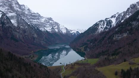Antena-Lenta-Acercándose-A-Un-Lago-Rodeado-De-Montañas-Nevadas-En-Los-Alpes,-Suiza