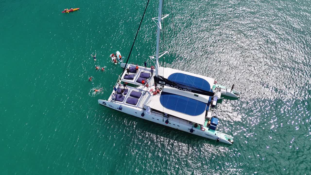 Aerial view of a catamaran with people swimming nearby in Phuket's turquoise sea, showcasing a serene tropical escape