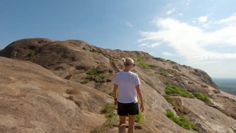 A-slow-motion-shot-tracking-from-behind-a-blonde-western-lady-as-she-climbs-up-stairs-on-a-granite-mountain-in-East-Africa