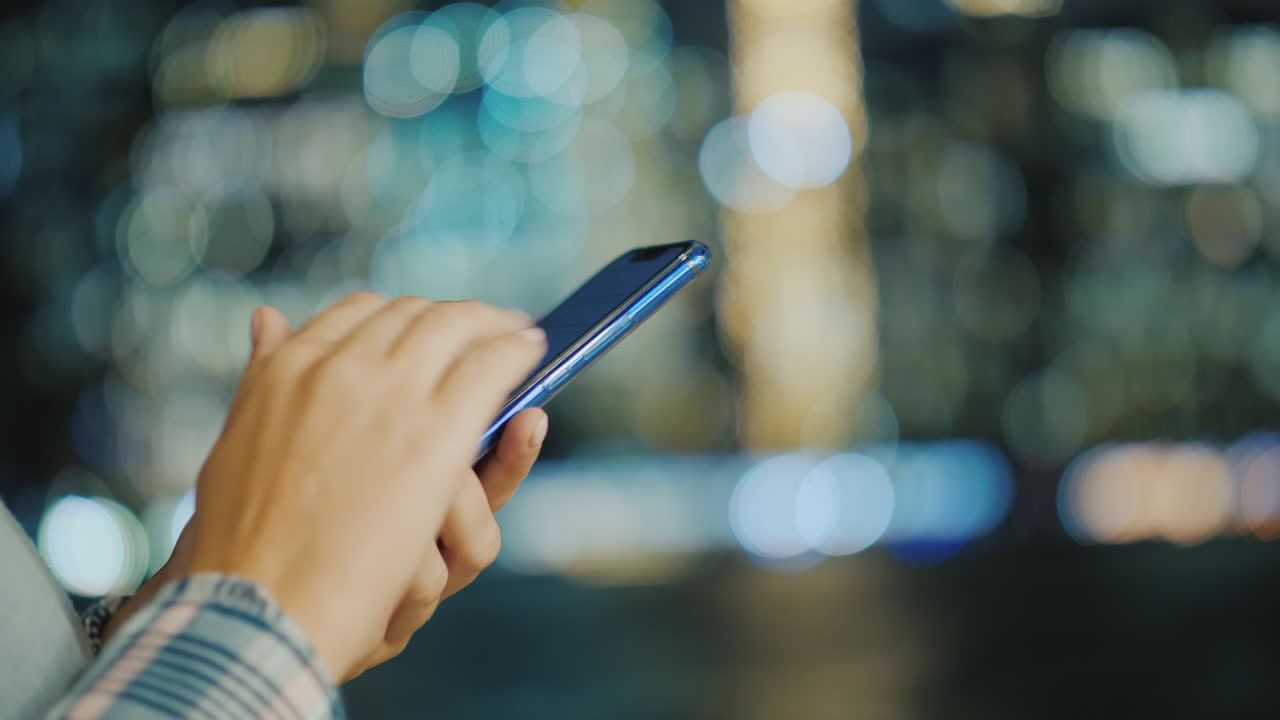 manos de una mujer joven con un teléfono inteligente en el fondo de las luces divididas de la ciudad
