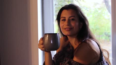 Hermosa-Mujer-Feliz-Con-Una-Taza-De-Café-Sentada-En-El-Alféizar-De-La-Ventana