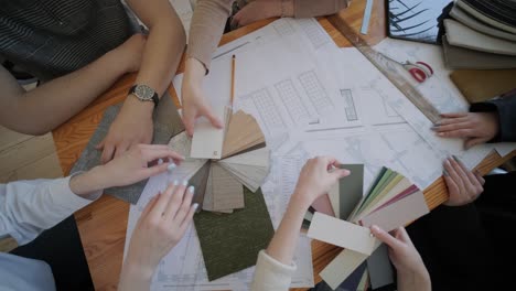 un equipo de diseñadores de interiores colabora en una mesa, examinando planes arquitectónicos, muestras de tela y paletas de colores, planeando un proyecto de diseño