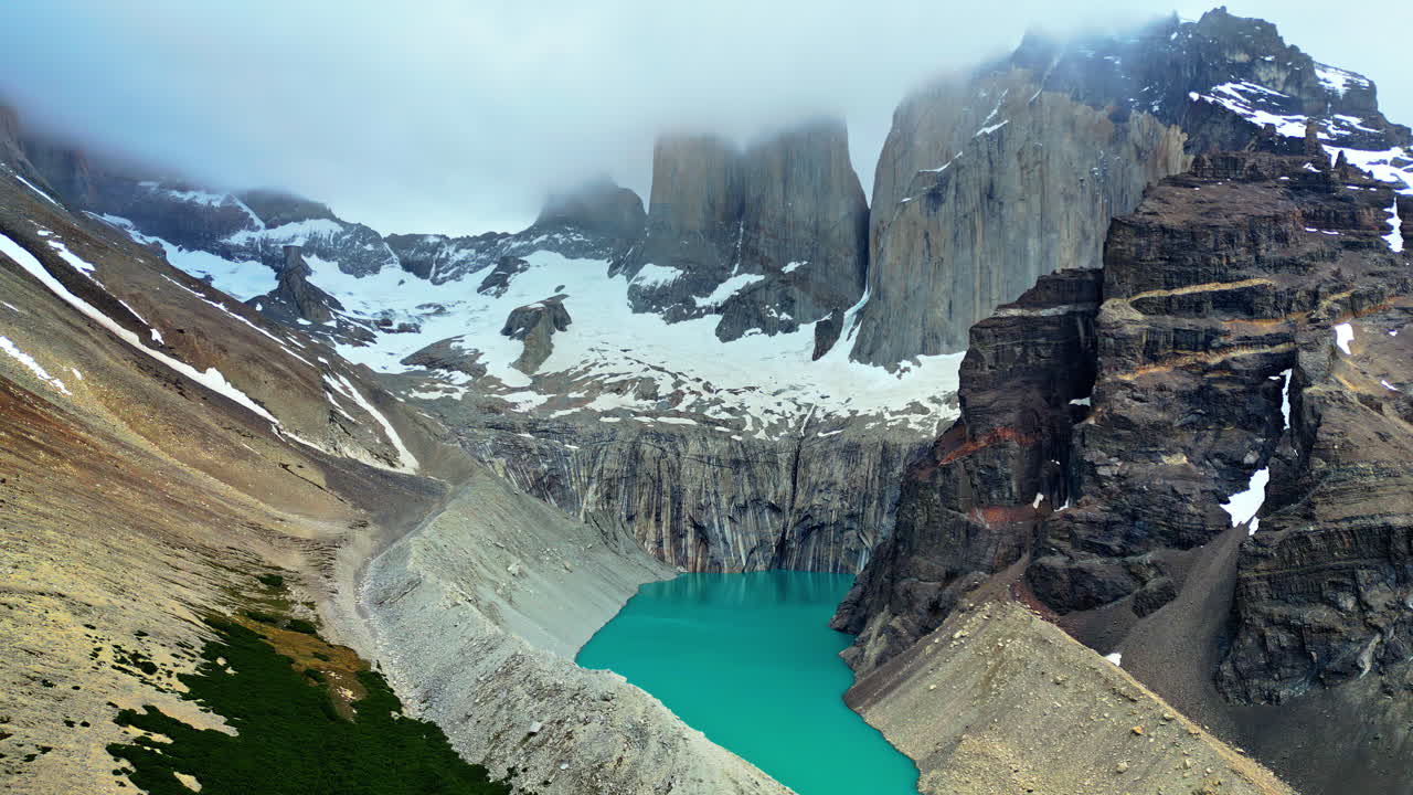 Vista aerea con drone delle iconiche torri del Paine che si ergono su un lago turchese circondato da neve e ripide scogliere