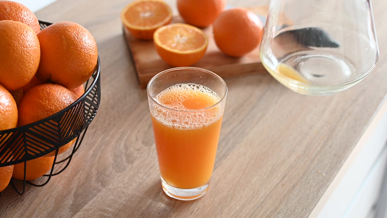 Mand hælder appelsinjuice i et glas i køkkenet