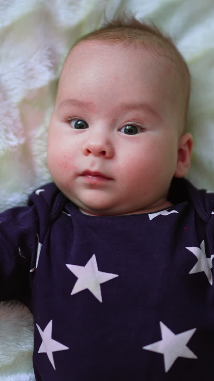 Happy cheerful healthy kid on the bed. Baby boy in dark sweater with stars on white backdrop. Close up. View from top. Vertical video