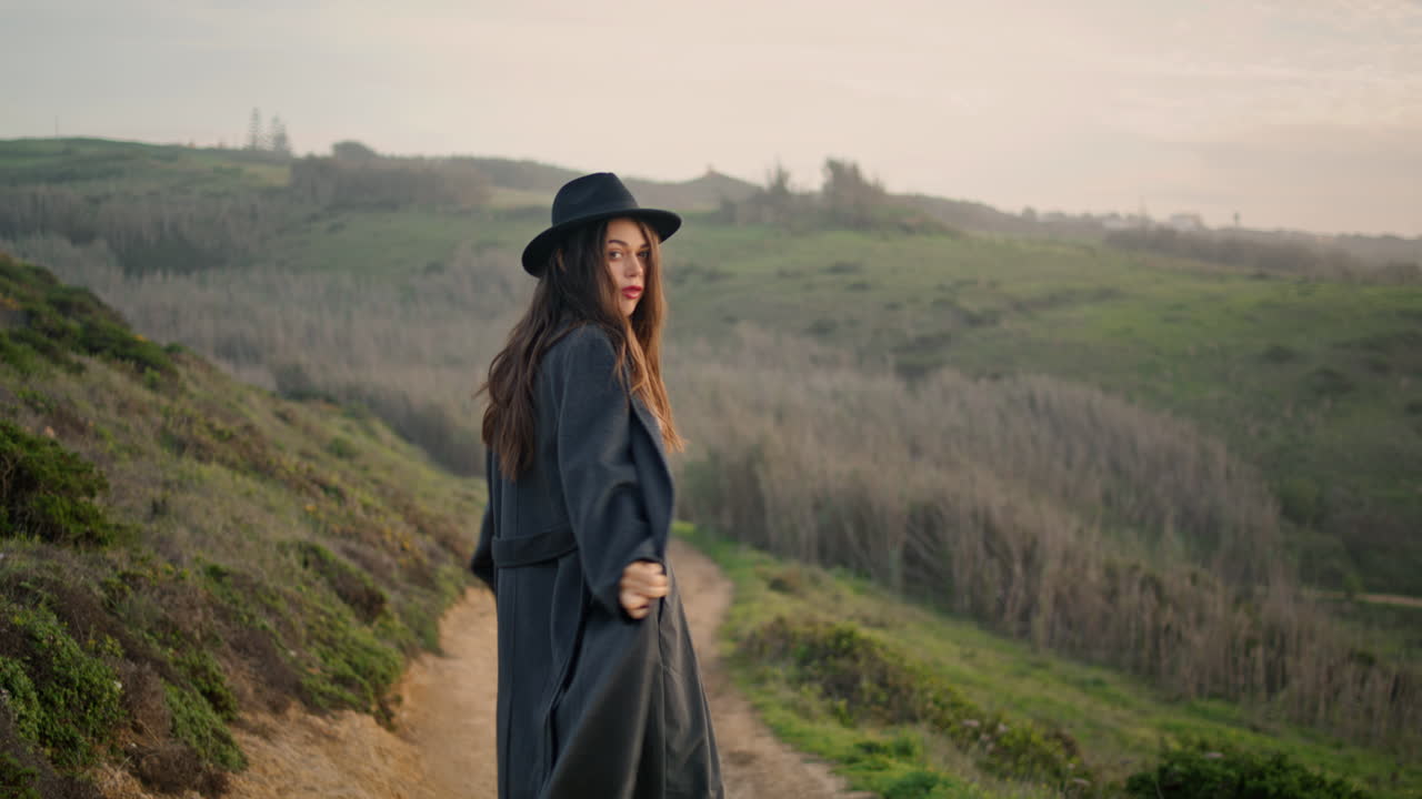 Donna viaggiatrice di spalle che cammina su una strada rurale. Ragazza che percorre un sentiero guardando indietro.