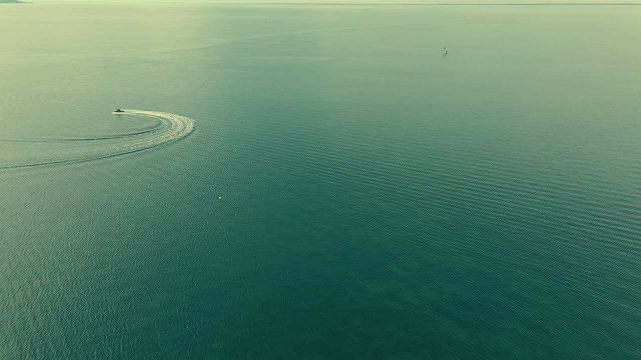 Aerial shot motorboat on left top corner floating on the sea, slow motion green clear water on trhe sea