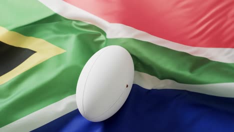 white rugby ball over waving flag of south africa with copy space, in slow motion
