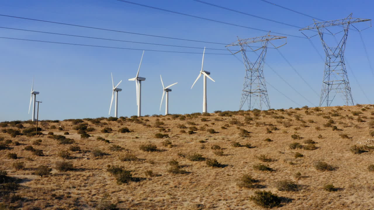 vista aérea panorámica de derecha a izquierda con vistas a las turbinas eólicas y la línea de transmisión de alto voltaje que revela un enorme parque eólico cerca de palm springs en el desierto de mojave, california, ee.uu.