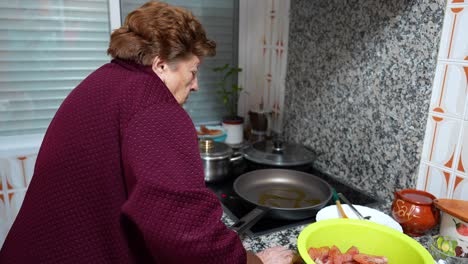 old granny cooking in the kitchen with olive oil in a fried pan