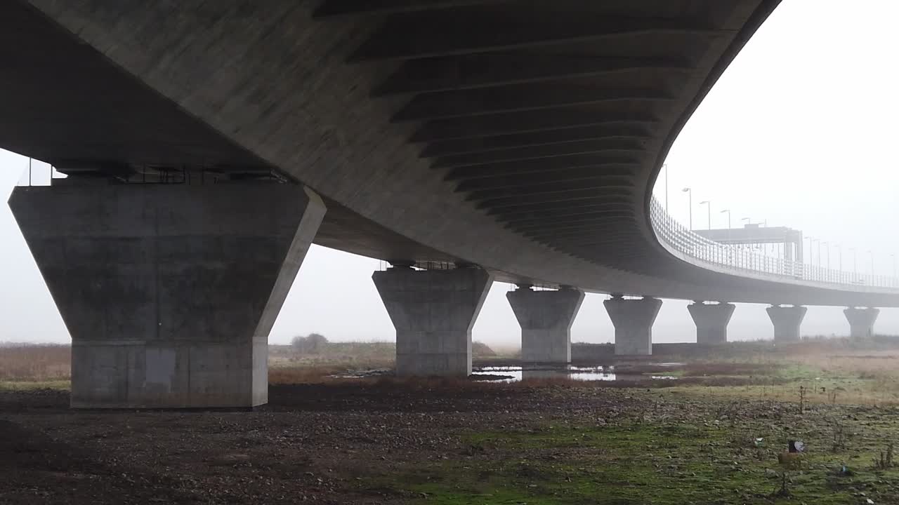 오른쪽으로 이동하는 고속도로 고가도로 아래의 안개 낀 콘크리트 지지 구조물