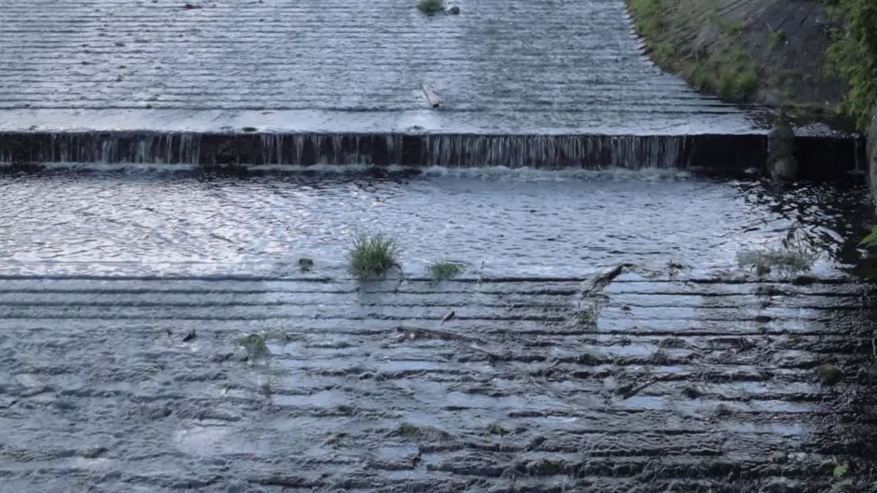 Weir at reservoir with water gushing over stones tilting shot