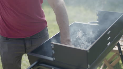 man standing at barbeque grill and touching coal smoke