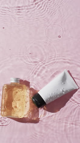 vertical video of beauty product tube and bottle in water with copy space on pink background