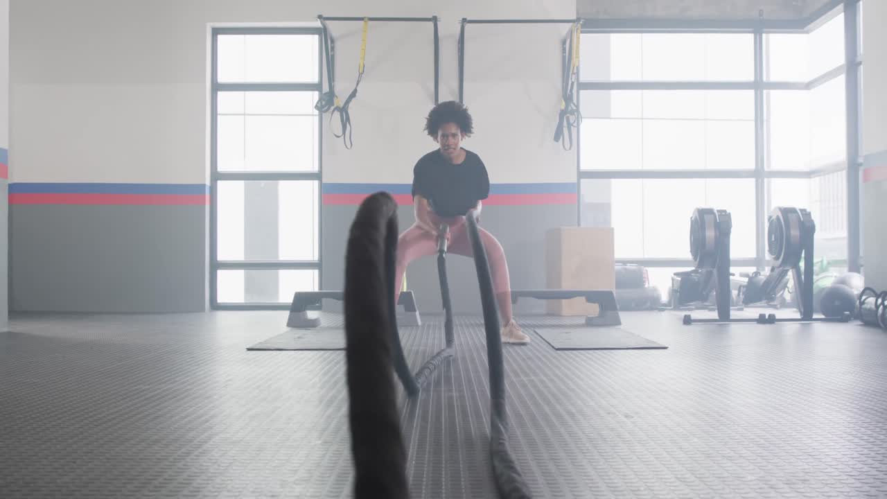 결심 한 아프리카계 미국인 여성 이 체육관 에서 싸우는 로프 를 사용 하여 운동 하는 영상
