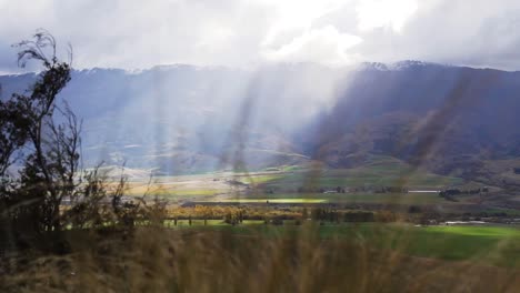 Revelación-Lenta-Del-Valle-Montañoso-Con-Rayos-De-Sol-Que-Se-Transmiten-Y-Plantas-En-Primer-Plano