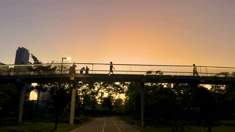 silhouetted figures walk across a bridge at sunset in benjakitti park, bangkok, with warm lighting and a tranquil atmosphere