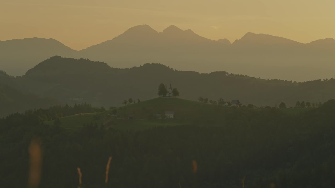 Couple hiking at sunrise near St. Thomas Church, Slovenia with scenic mountains in the background