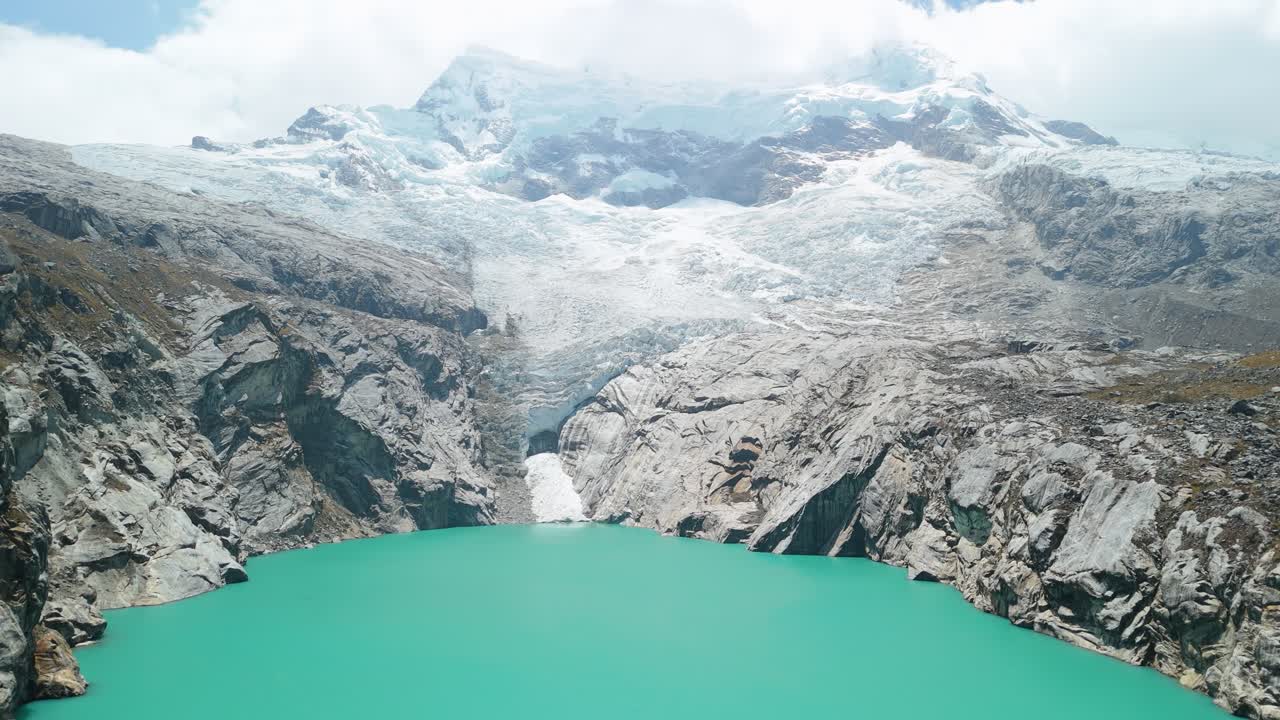 Aerial ascending shot closely follows a rugged rocky ridge leading toward the bright turquoise waters of Laguna 513 in the Peruvian Andes