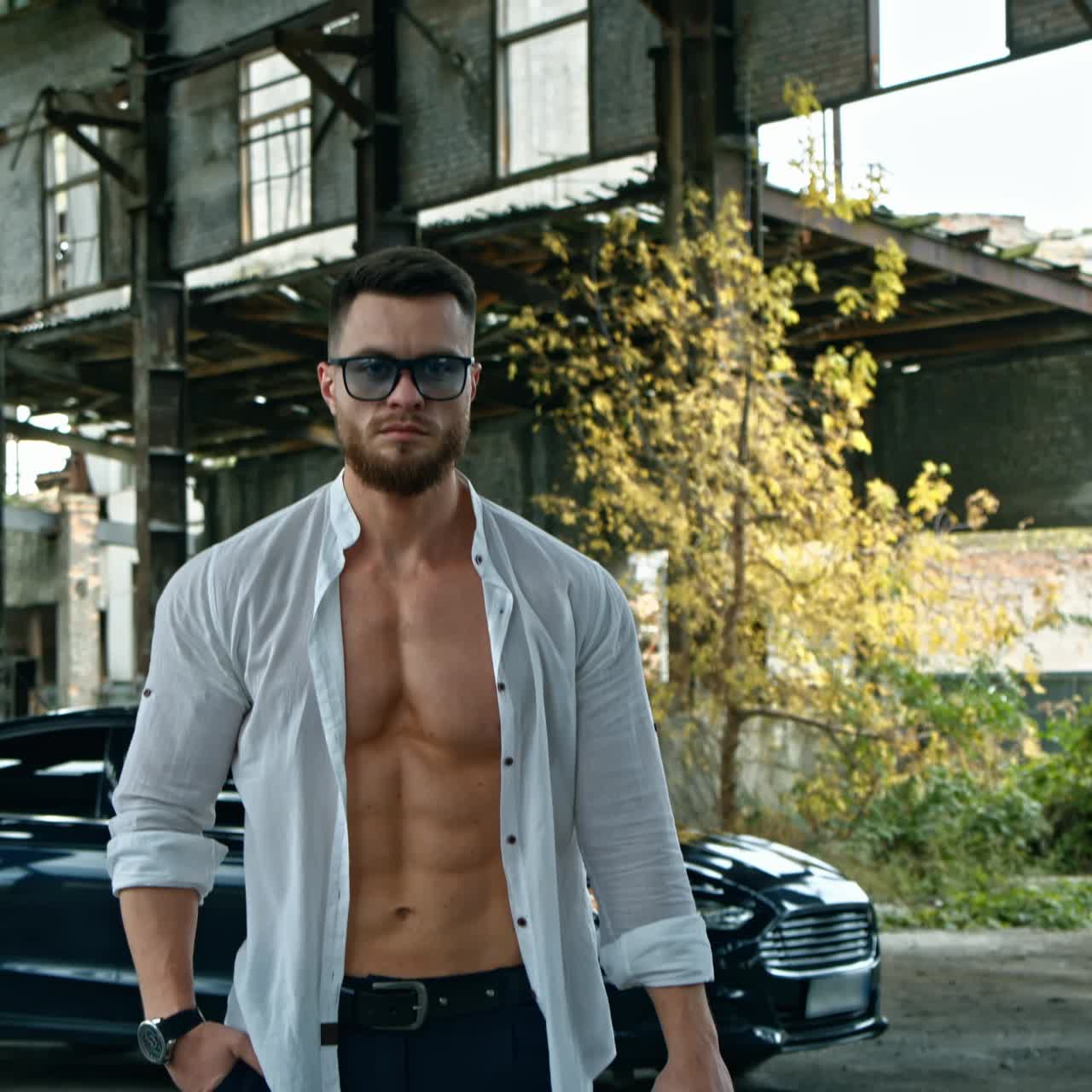 Businessman with a handgun. Young handsome man in shirt and glasses holds pistol in his hand. Serious man with sportive body with a weapon outdoors.