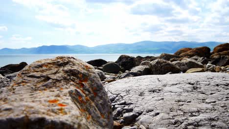 Colourful-variety-of-stone-boulders-beach-landscape-under-North-Wales-mountain-range-descending-jib-right