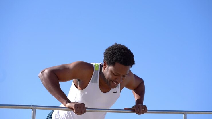 Happy muscular man doing push ups on bar against blue sky