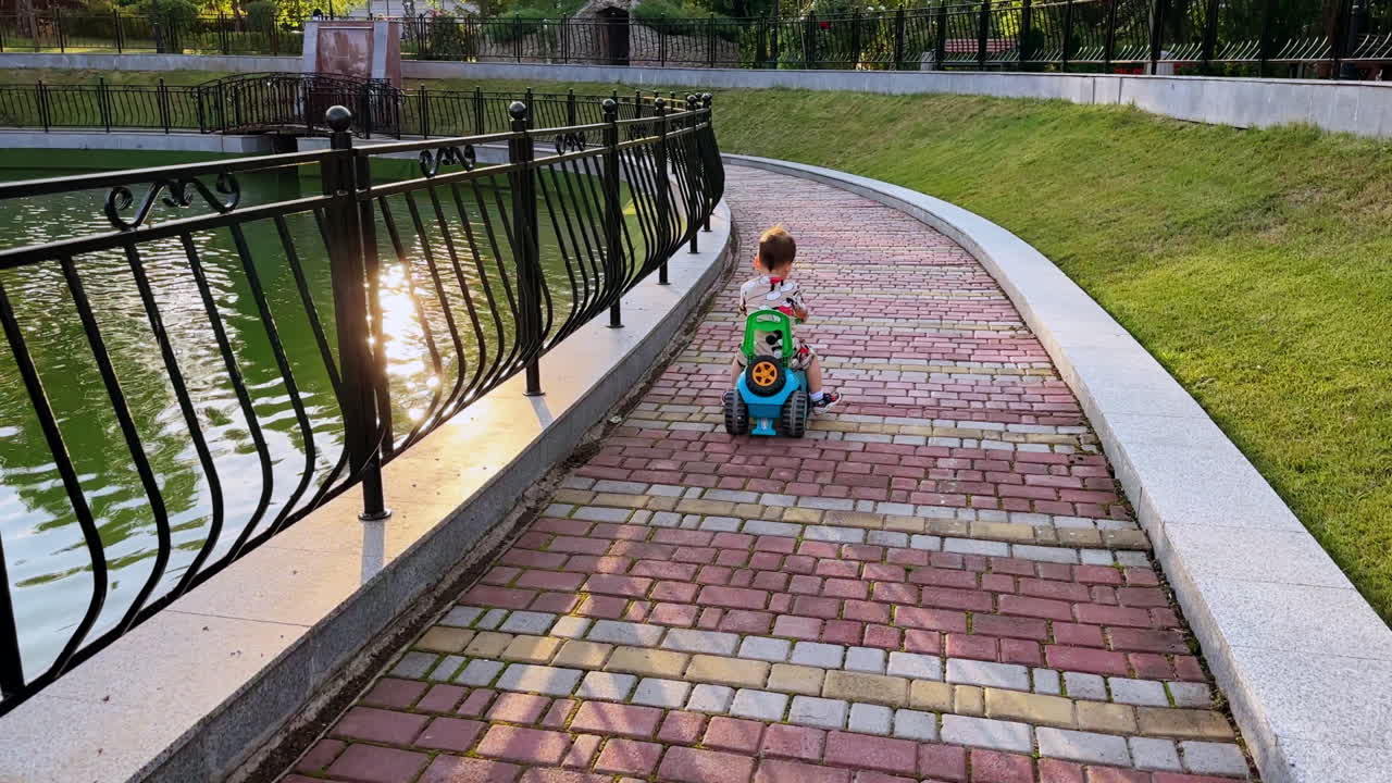 Following the little child riding his toy car quickly. Caucasian toddler in the park near the pond.