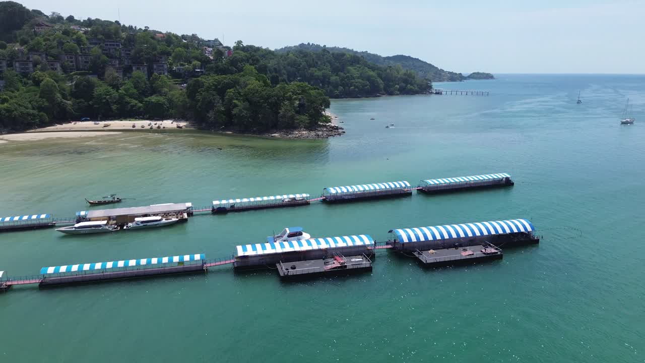 Smooth left-to-right drone shot over Patong Beach, showcasing colorful Thai taxi boats, clear turquoise waters, white sand, and the lively Phuket coastline.