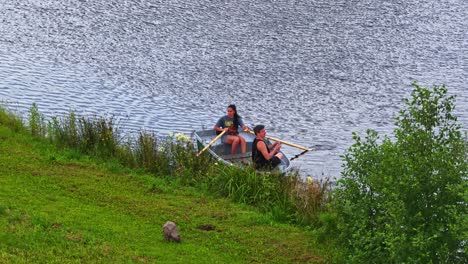 a young couple enjoys a summer day on a latvian lake, with the woman rowing a small boat while the man operates a drone controller to capture aerial footage