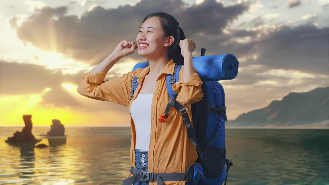 夕焼け時にビーチに立って成功を祝うアジア人女性ハイカーの側面図、登山用バックパックを持ち目標を叫ぶ