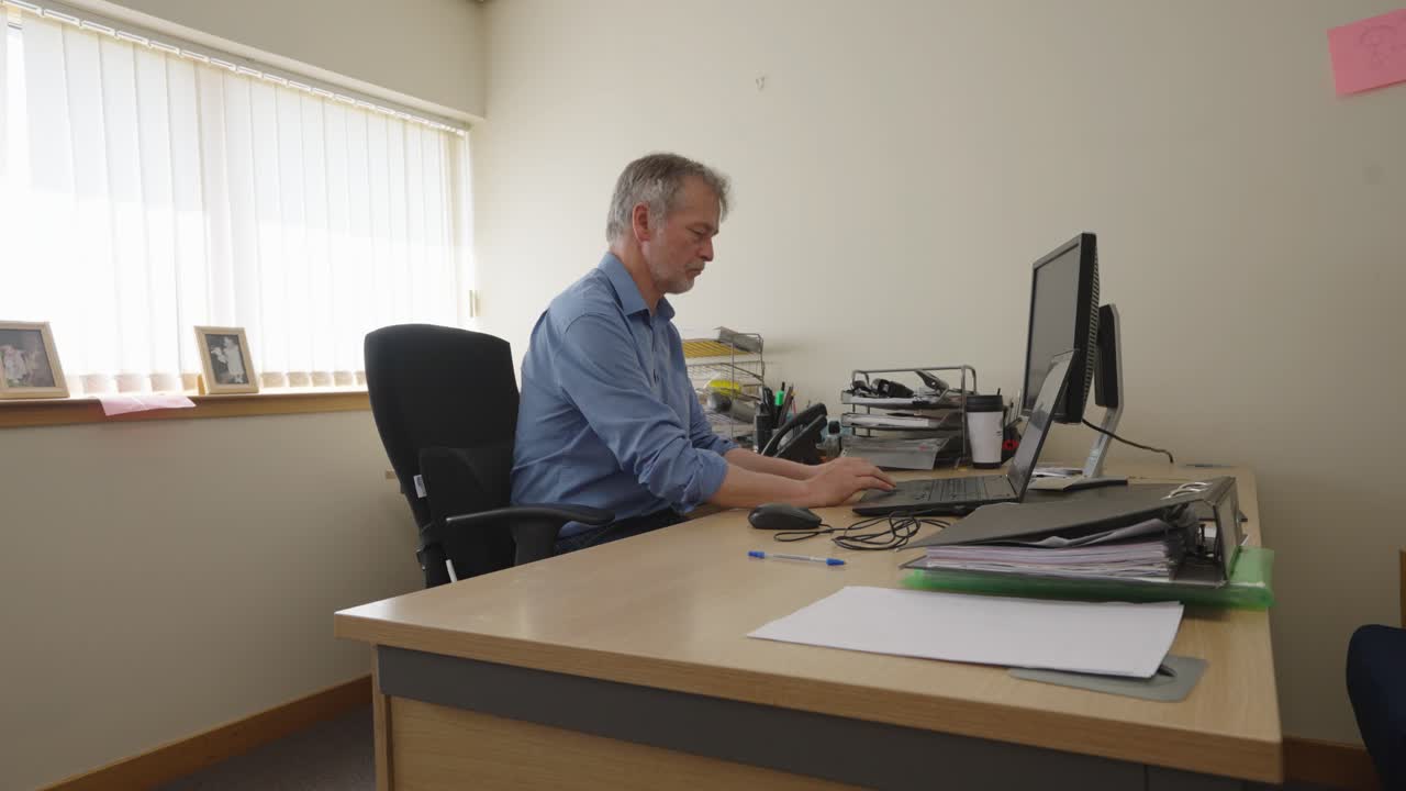Man in blue shirt making phone call and working in an office, locked off