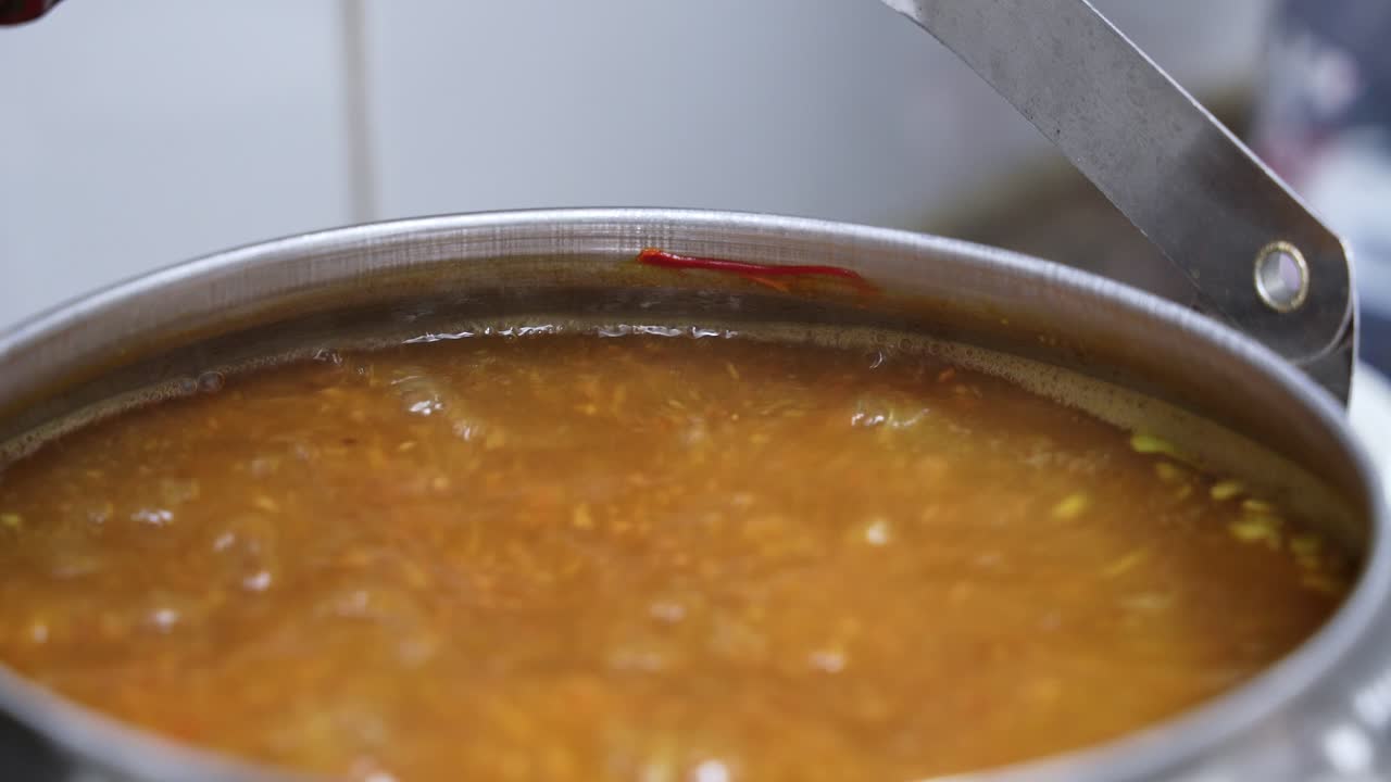 Tè speziato tradizionale o caffè arabo che sobbolle in una pentola di metallo. Pezzi visibili di zafferano e cardamomo nel liquido arancione bollente durante una sessione di cucina casalinga.