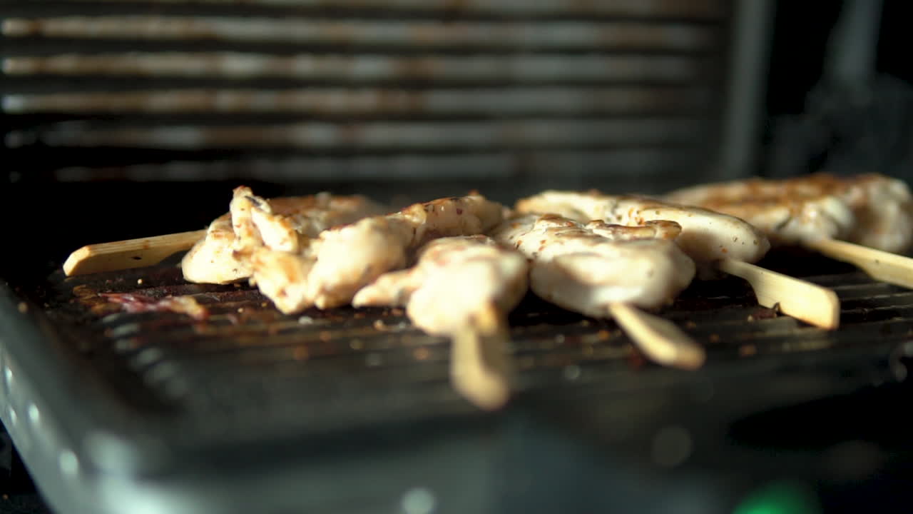 Pieces of chicken sirloin stuffed onto a wooden stick lie on the grill - Slow motion smoke from grate