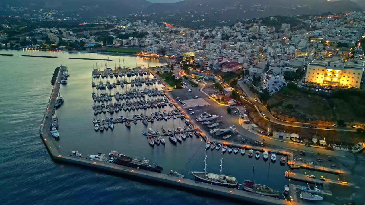 Aerial view of a coastal city of Agios Nikolaos at dusk, illuminated marina