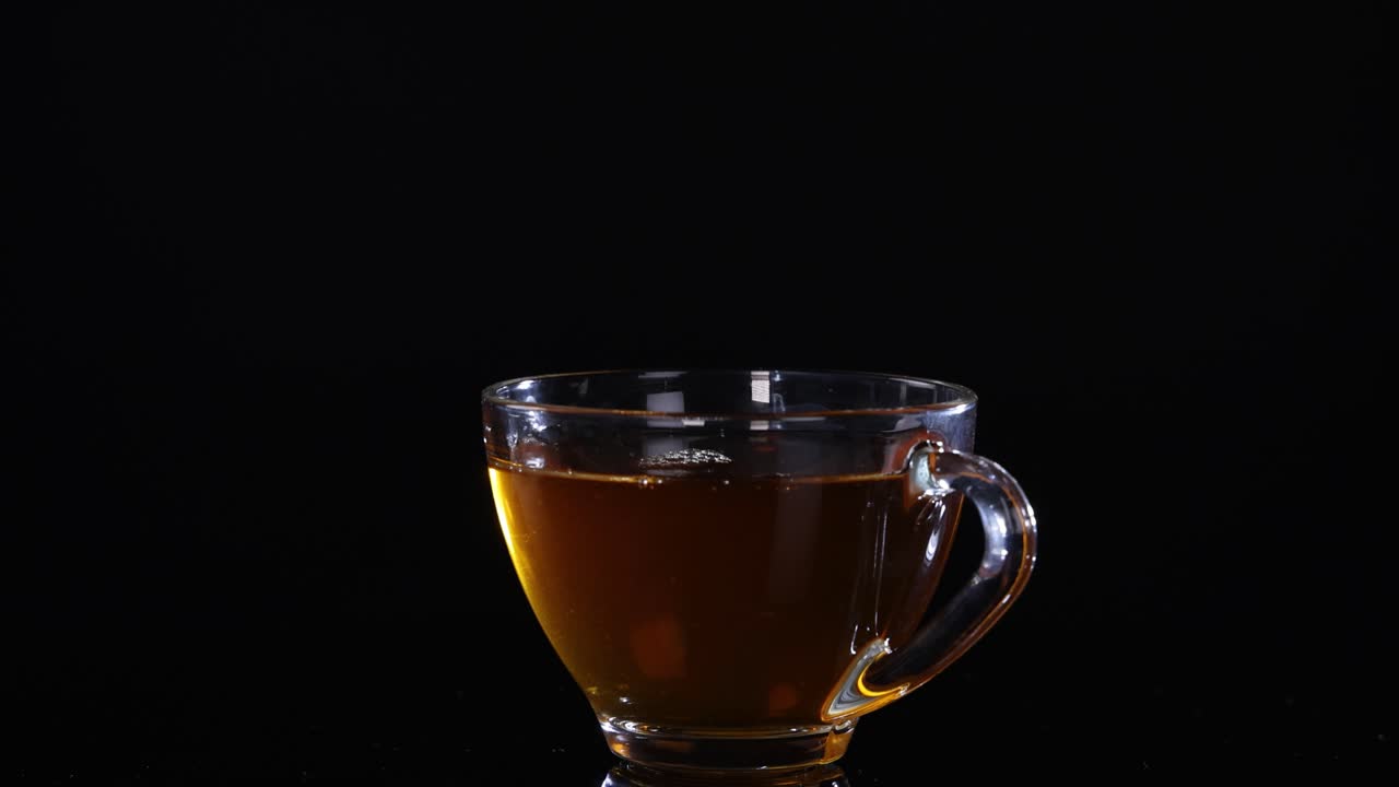 A glass cup filled with tea is centered against a black background, highlighting its warm color and transparency