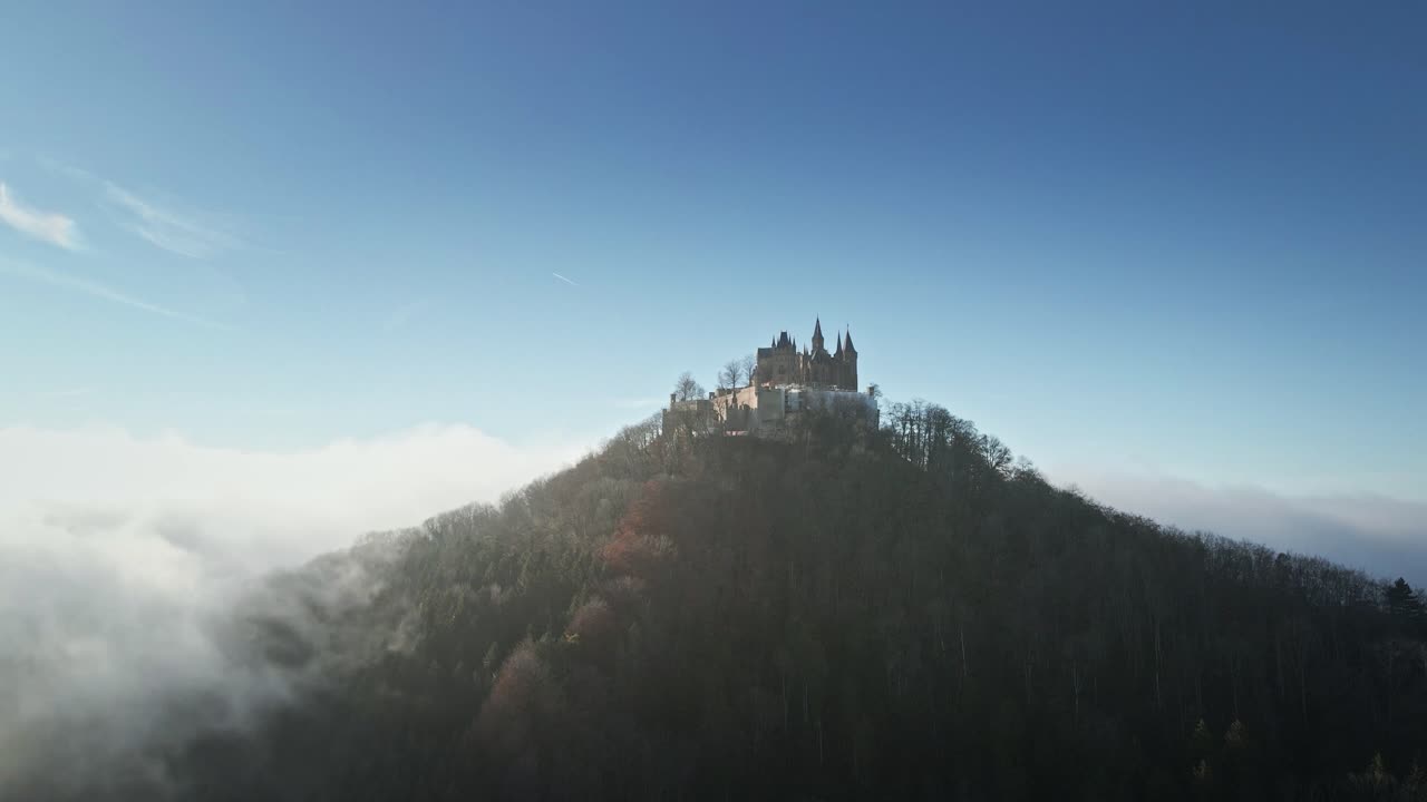 The drone orbits left around Hohenzollern Castle, gradually rising above the clouds, unveiling a breathtaking aerial view of the historic fortress and the misty German landscape.