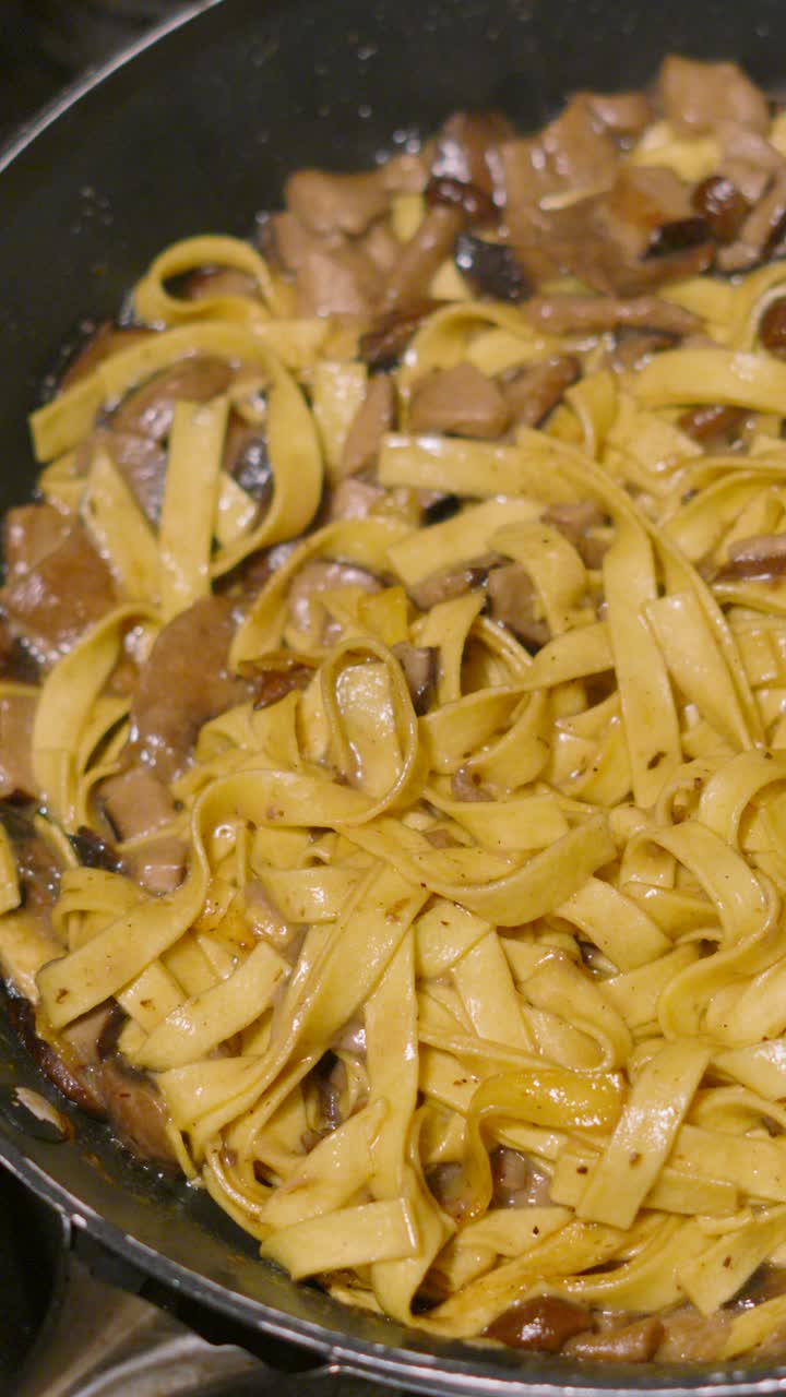 Vertical Overhead Video of Fresh Mushroom Tagliatelle Simmering in Hot Pan with Various Fungi Including Champignon, Shitake, Nameko. Home Cooked Cream Sauce Based Pasta Dish.