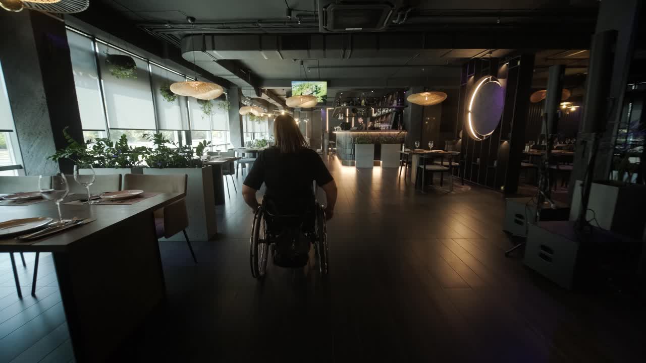 체어에 앉은 한 여성이 현대적인 장식과 예술적인 요소를 가진 세련되고 희미하게 조명된 레스토랑에 들어갑니다.이 장면은 유행의 식사 환경에서 접근성을 강조하며 이동성과 포적 인 디자인을 강조합니다.