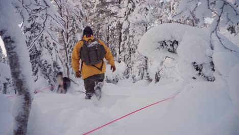 Man-Walking-In-Deep-Snow-With-Pet-Dog-Siberian-Husky-Running-On-A-Winter-Day