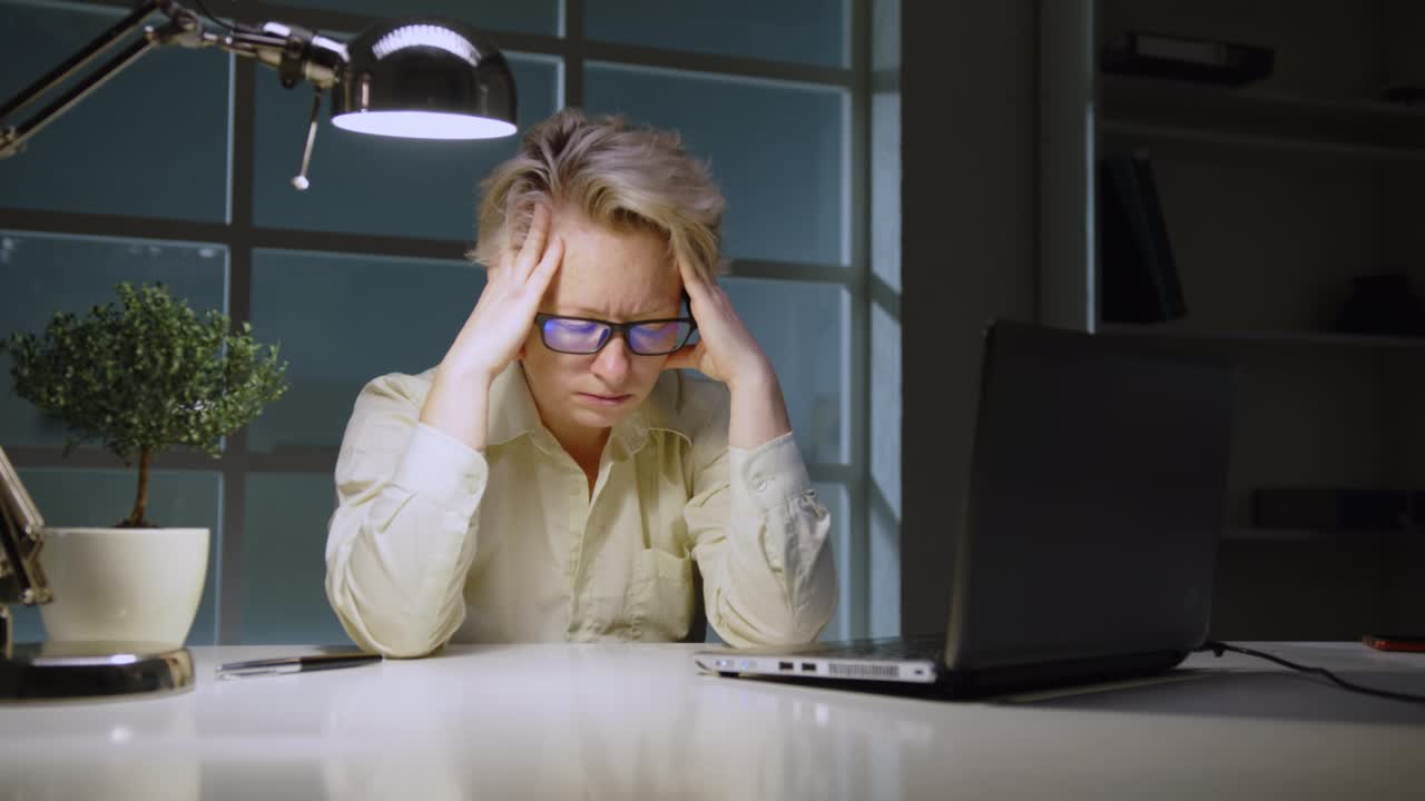 Upset woman manager is having headache while sitting at desk in office late at night, financial problems, bankruptcy