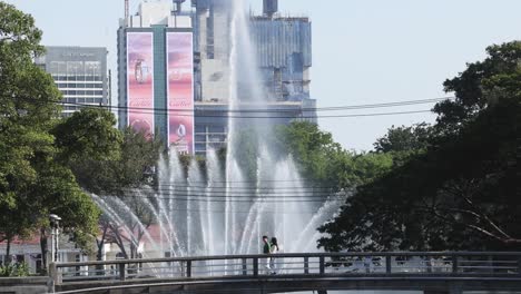 a vibrant fountain show set against towering skyscrapers and lush greenery in an urban park.