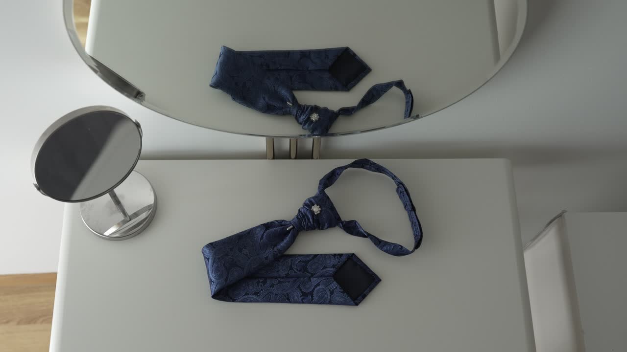 Blue patterned necktie with brooch, elegantly laid on a white surface and reflected in a mirror