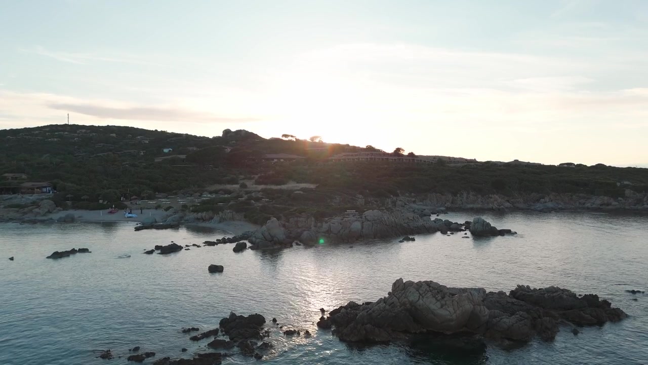 Veduta aerea di costa rocciosa e mare calmo all'alba vicino a rigogliose colline sarde