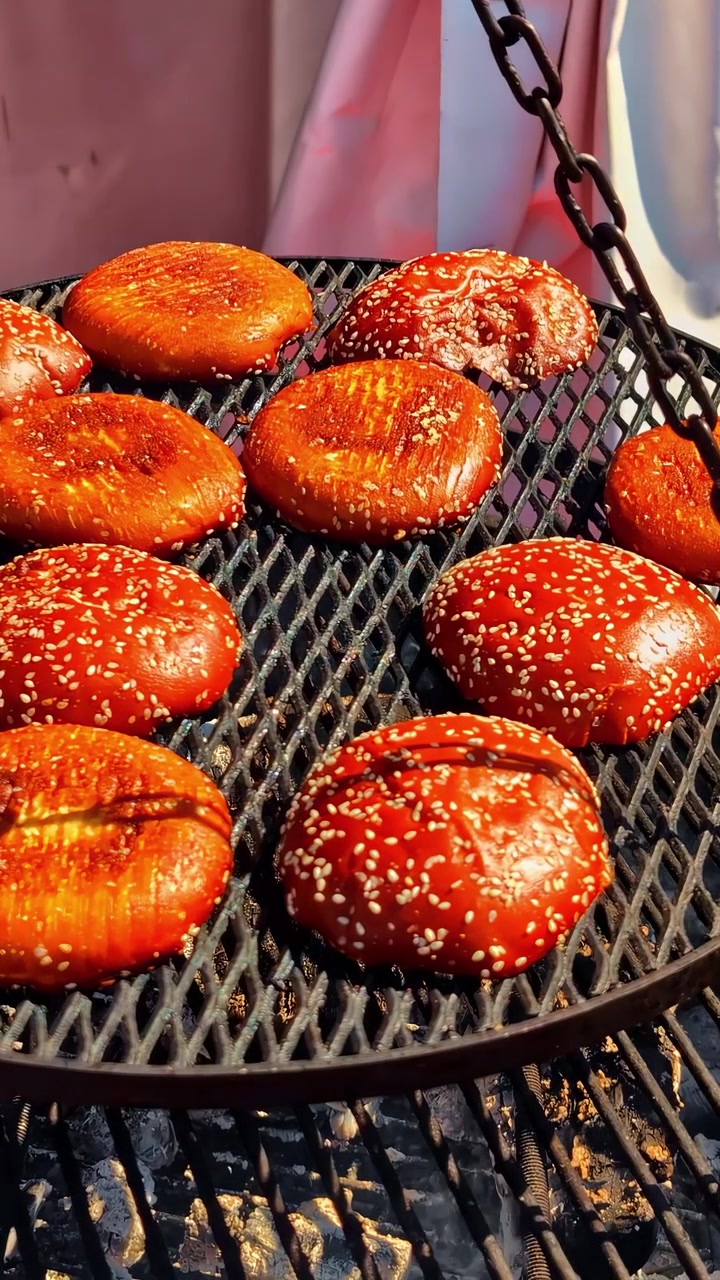 Sesame topped burger buns grilling over open fire on a rustic barbecue rack