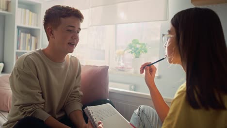 Two-caucasian-teenagers-sitting-on-bed-and-learning-from-books-with-smile