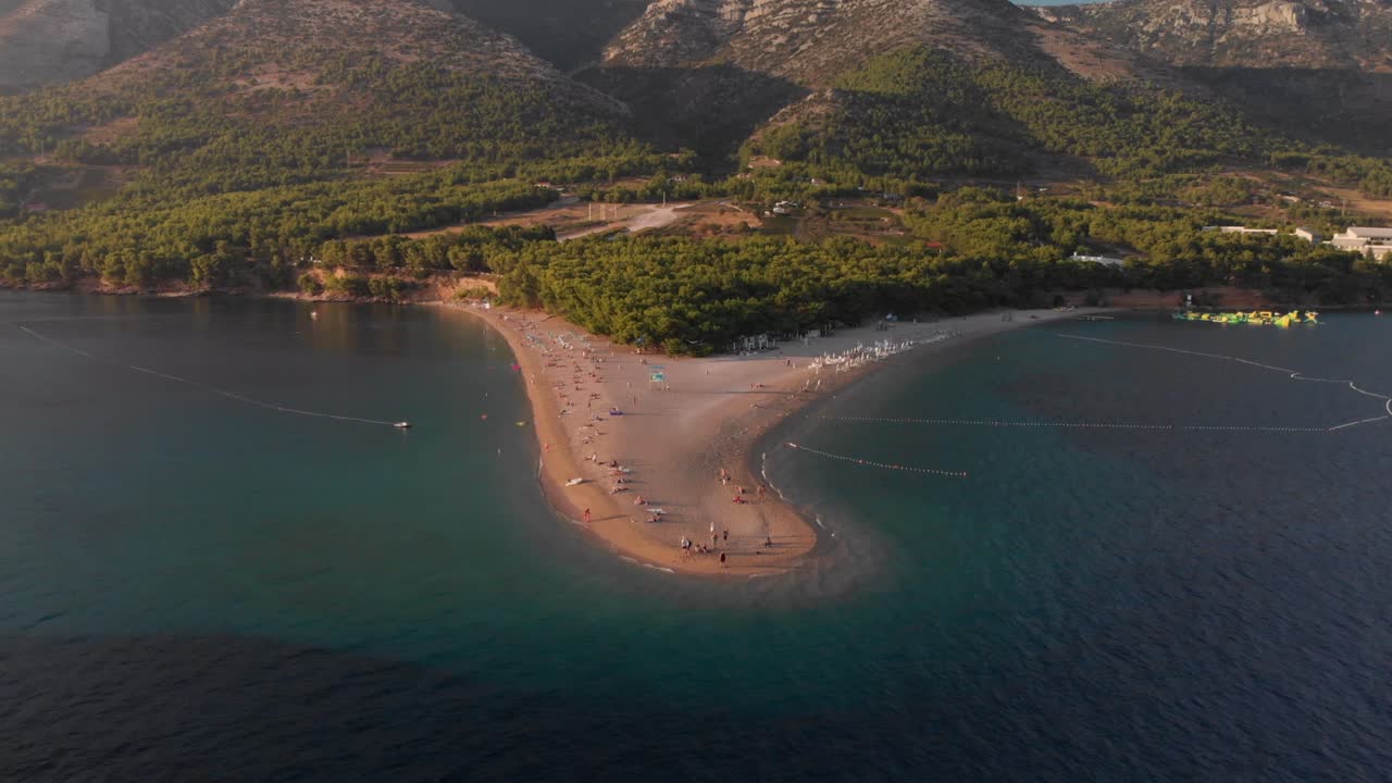 Slowly flying toward the beachhead of Zlatni Rat on the island of Brac in Croatia, tilting down as the drone approaches the beach