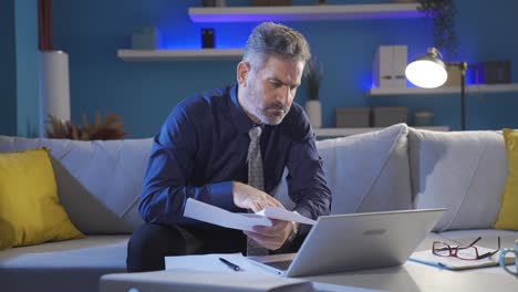 Focused-businessman-carefully-reading-document,-working-papers-and-laptop-seriously-and-professionally.