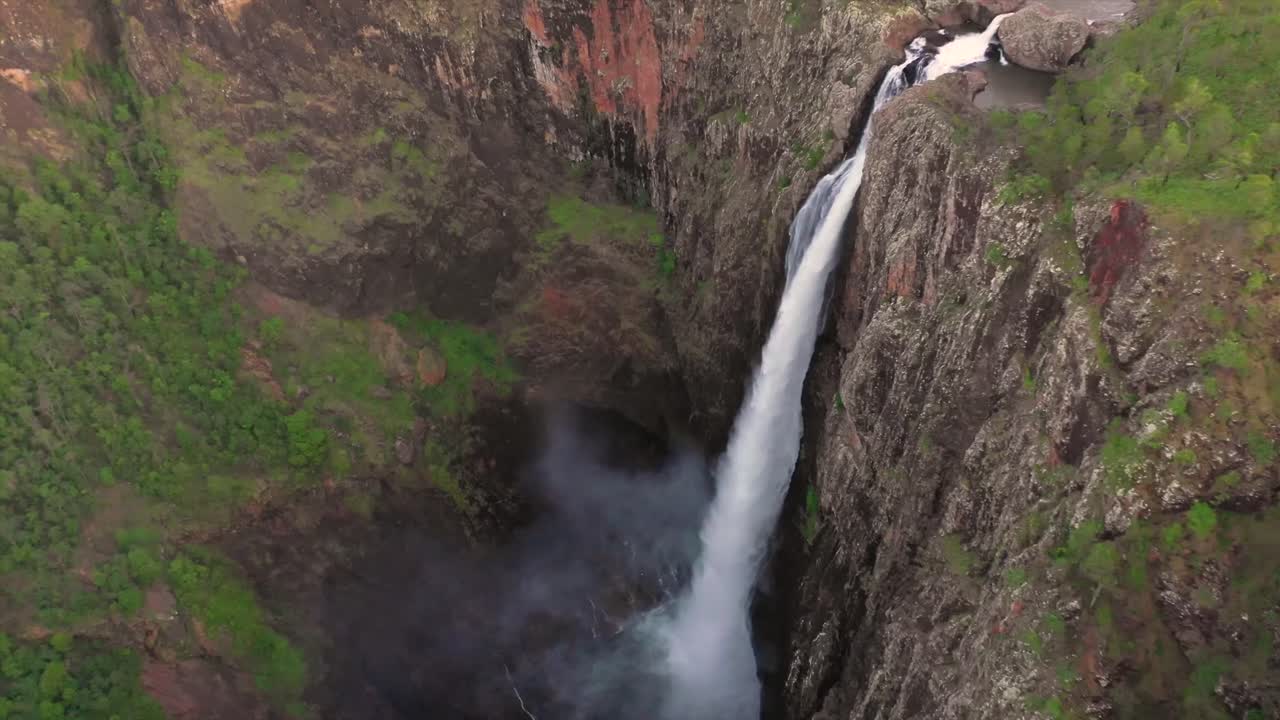 Vista aerea di una stretta cascata che si tuffa attraverso ripide scogliere rocciose a Sagres, sulla costa dell'Algarve, Portogallo, mostrando la caduta verticale dell'acqua, la nebbia, l'erosione e la drammatica geologia costiera.