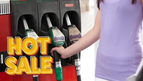 Animation-of-hot-sale-text-in-orange-over-midsection-of-woman-holding-fuel-pump-at-petrol-station