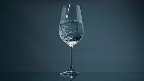 pure water filling glass at dark background closeup. bubbles rising transparent